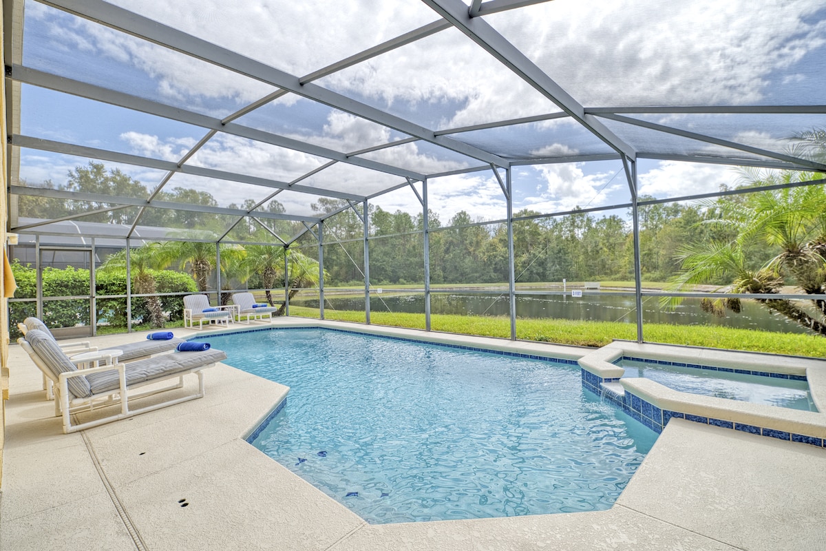The outdoor pool area features a screened enclosure that offers views of the surrounding greenery. A spacious pool with a spa is complemented by lounge chairs and a shaded area, providing options for relaxation and sunbathing.