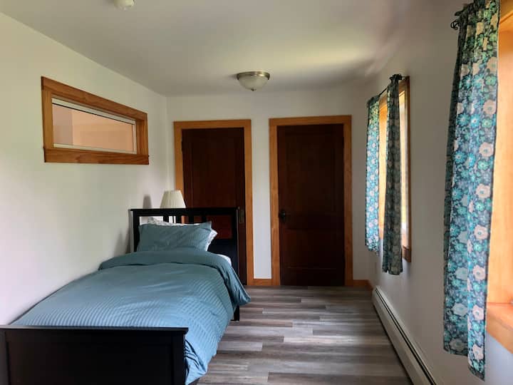 La chambre du deuxième étage dispose de deux lits jumeaux, de deux placards, de deux fenêtres et d'un ventilateur au plafond. Vue d'un lit jumeau devant deux placards.