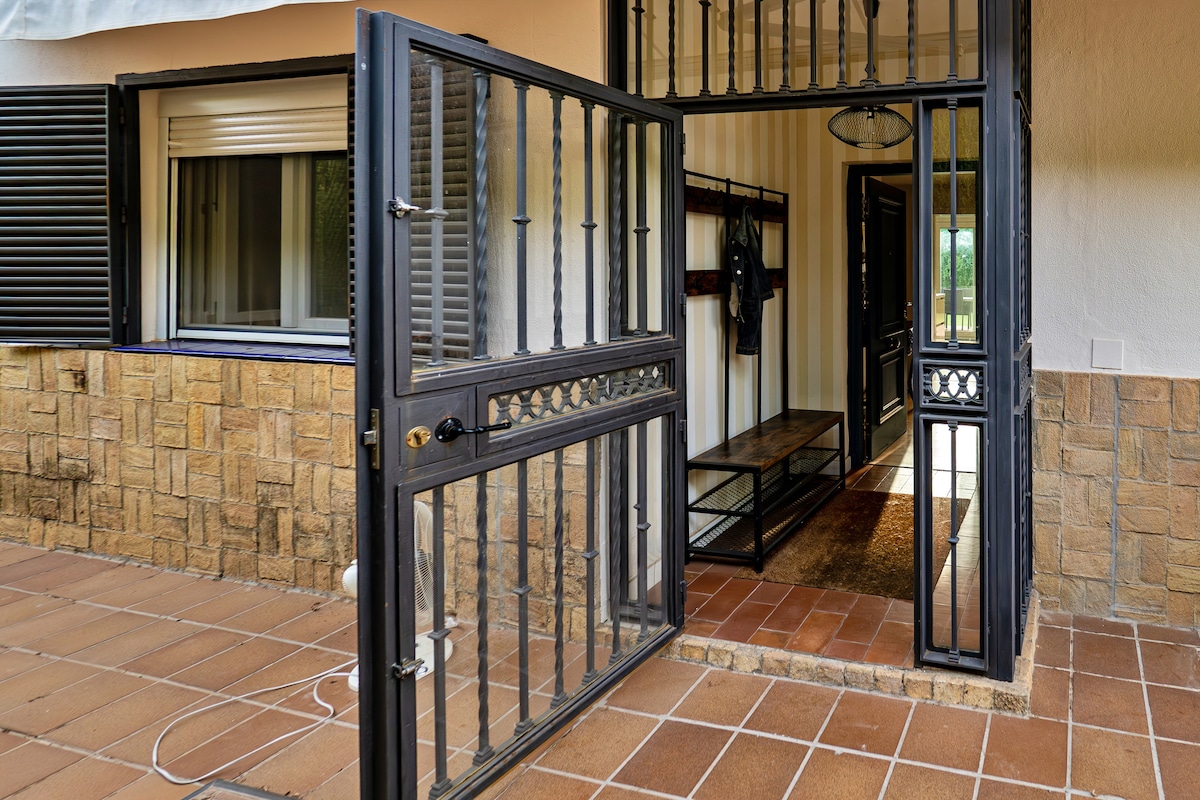 The entrance features a black wrought iron gate complemented by a stone wall and tiled flooring. A spacious foyer is visible, with a built-in bench and hooks for hanging items, allowing for easy access and storage upon entry.