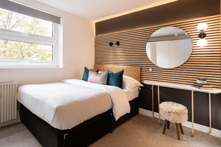 A double bed with bespoke headboard with built in lights, usb charging ports and a dressing table