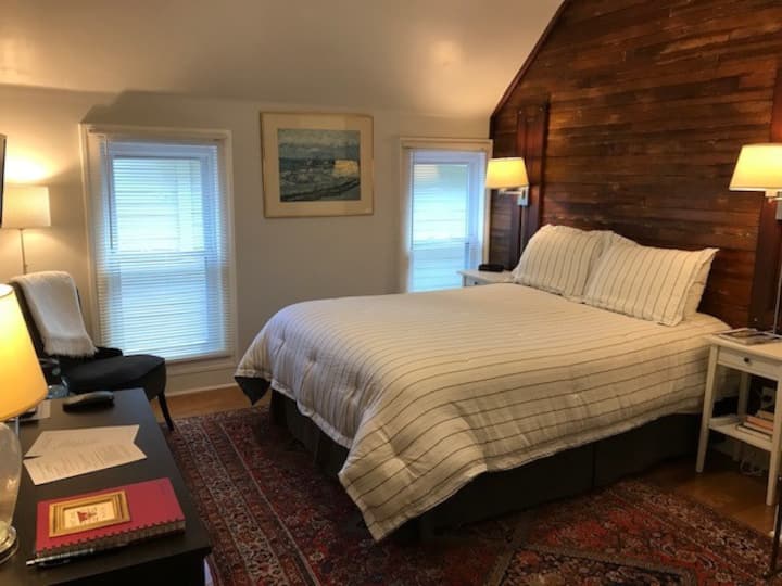 The bedroom has a queen-sized bed and is spacious and bright. The headboard wall features the flooring removed when the entire second floor was renovated.