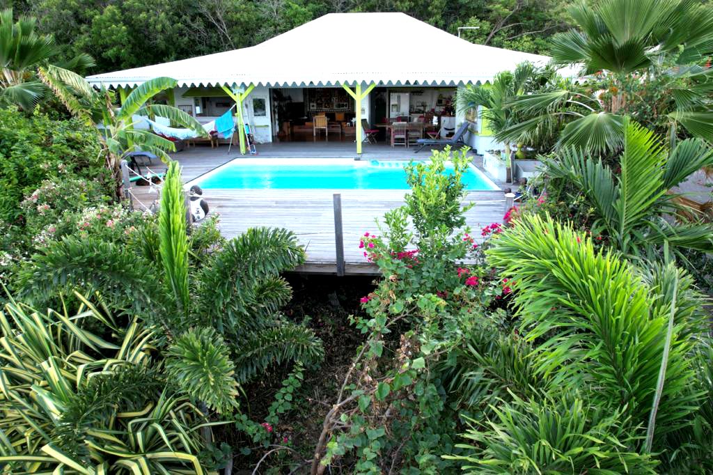 A serene outdoor area features a swimming pool framed by lush tropical plants and vibrant flowers. The covered terrace offers seating arrangements and views of the pool, while the surrounding greenery enhances the natural ambiance.