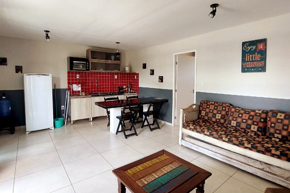 An open living area features a comfortable sofa bed, a dining table, and a well-equipped kitchen highlighted by red tiled backsplash. The space is complemented by a compact refrigerator and cooking essentials, all arranged within a bright, welcoming environment.