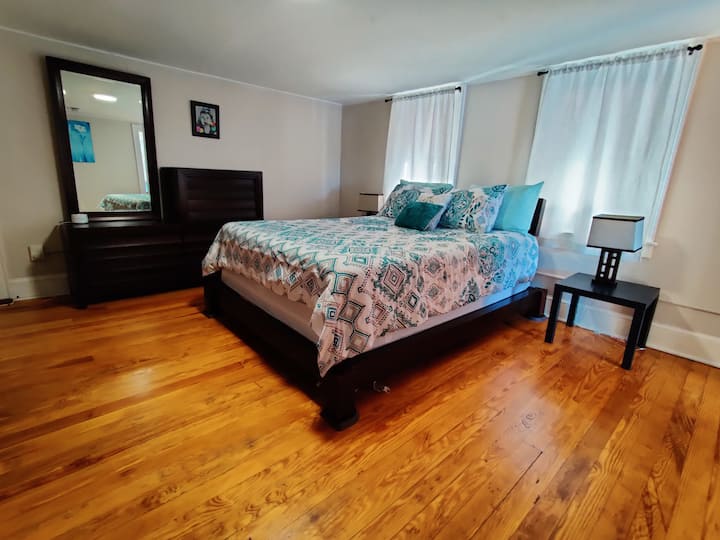 Large bedroom with queen bed, dresser, side table, mirror