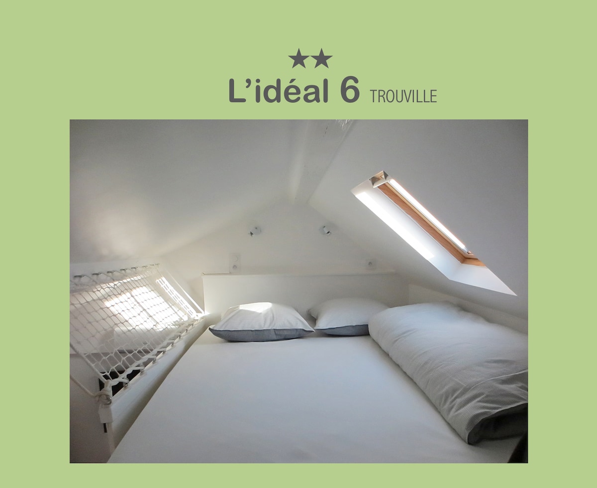 A cozy mezzanine sleeping area features a spacious bed with soft pillows and linens. Natural light filters through a small skylight, enhancing the bright and airy atmosphere. The room is nestled in a sloped ceiling, accented by a subtle netting detail for added charm.