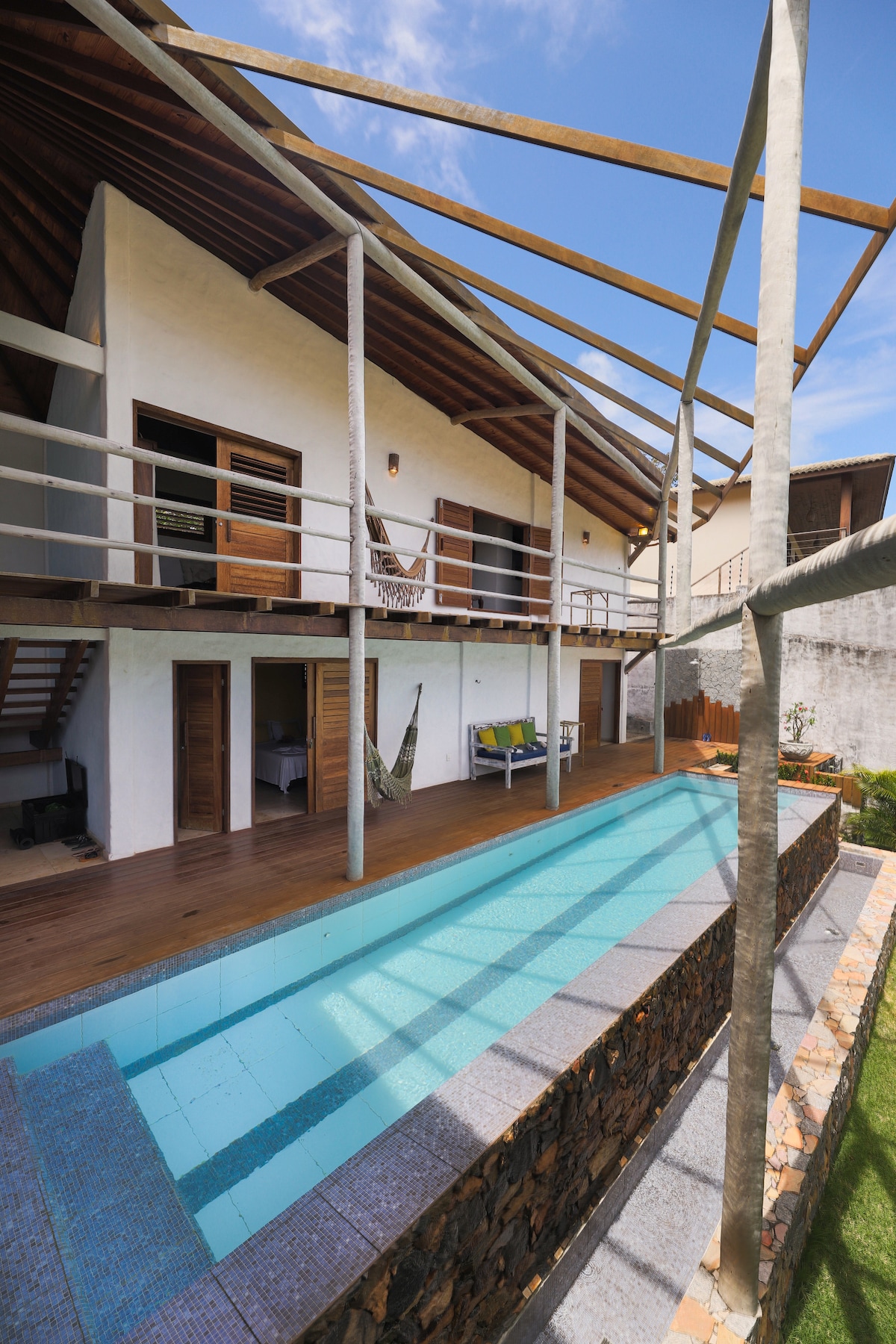 A modern villa is presented, featuring a spacious outdoor area with a pool. The upper level showcases a balcony with wooden railings, while the ground floor offers sliding doors leading to the pool. A well-kept garden borders the pool, enhancing the outdoor environment.