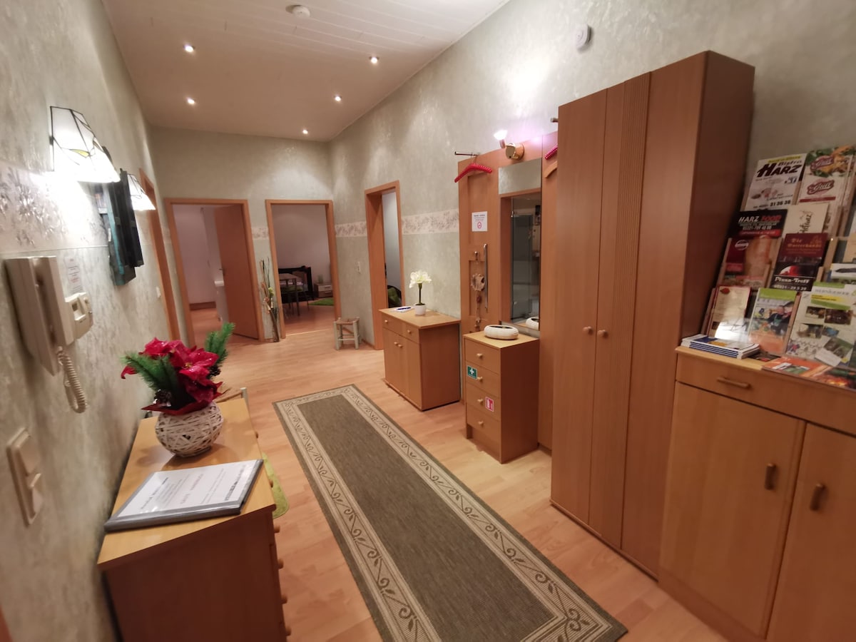 A well-lit hallway features wooden cabinets and shelves, providing storage and display for brochures and information. A decorative flower arrangement enhances the welcoming atmosphere, while a long runner rug adds a touch of warmth to the wooden floor.
