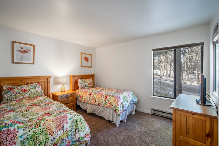 Спалня 2 предлага две единични легла, телевизор и много естествена светлина от големи прозорци, създавайки светло и приветливо пространство за почивка и релаксация.