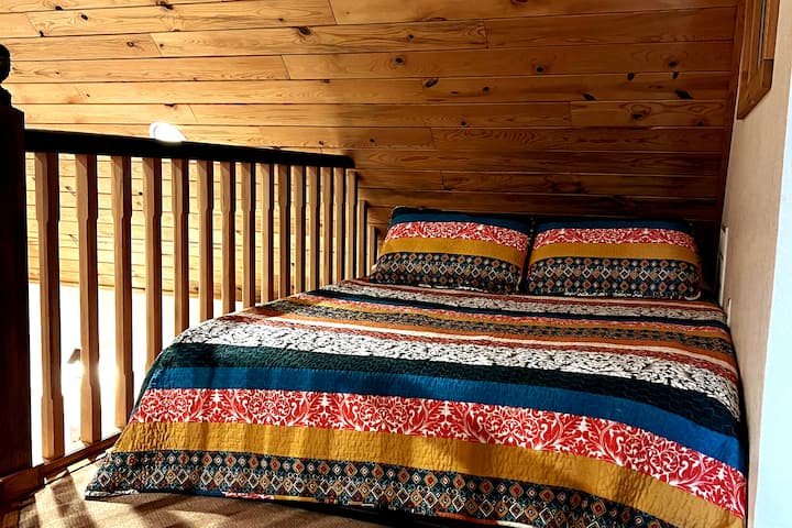 يوجد سرير كامل منخفض في مساحة علوية مفتوحة مريحة، خارج غرفة النوم الرئيسية مباشرة.