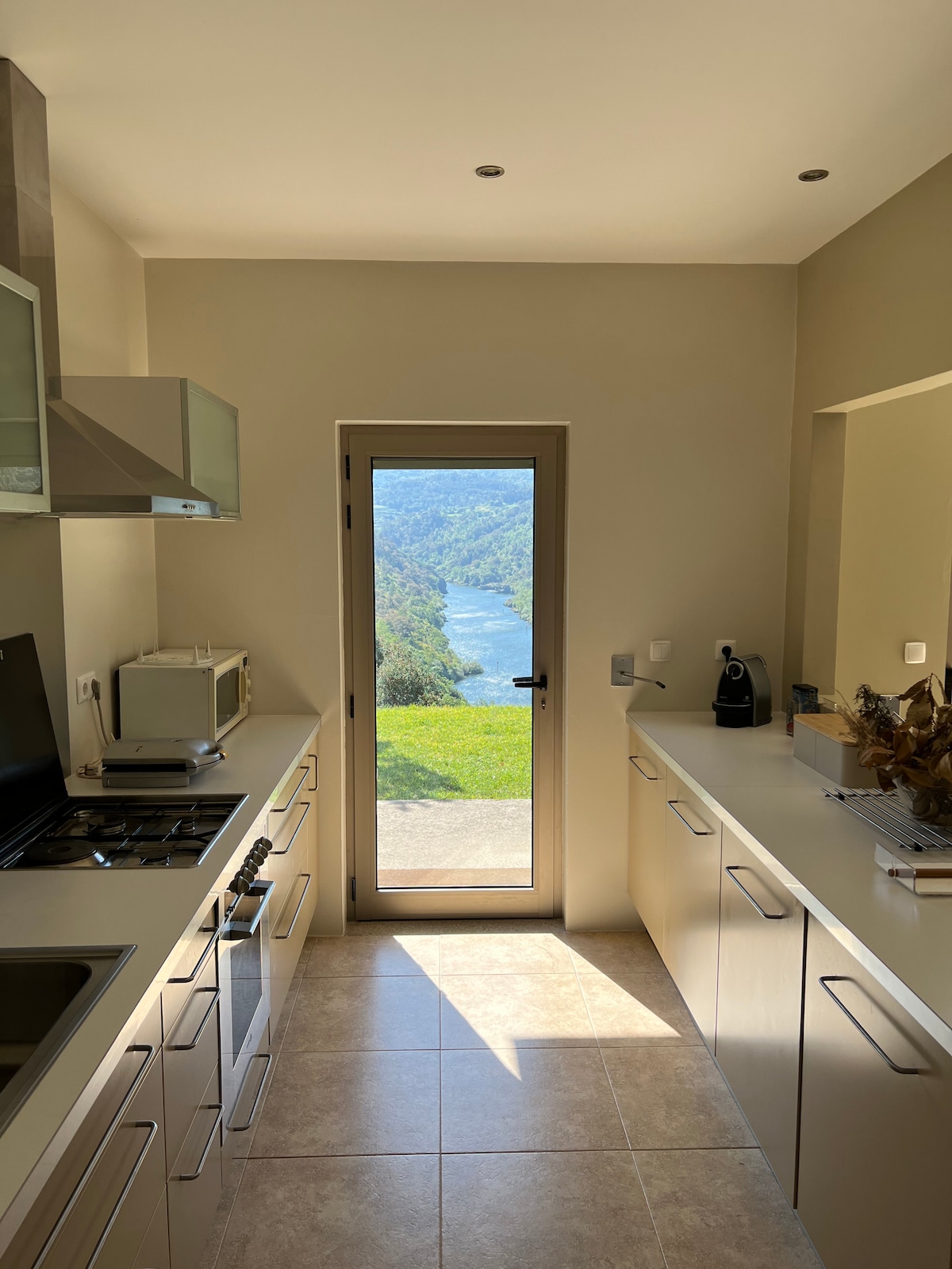 A modern kitchen is showcased with sleek cabinetry and stainless steel appliances. Large windows open to a panoramic view of the Douro River and surrounding landscape. Natural light brightens the space, illuminating the countertops and creating an inviting atmosphere.