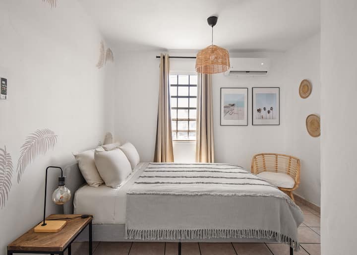 Vista al dormitorio con aire acondicionado, cama tamaño queen con sábanas de algodón y cómodo colchón