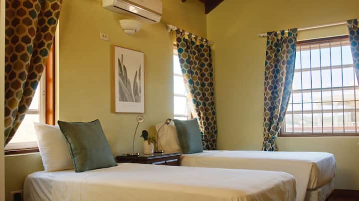 Slaapkamer 1 - 2 eenpersoonsbedden met een badkamer en suite, kastruimte, airconditioning, een plafondventilator en gedeeld balkon.