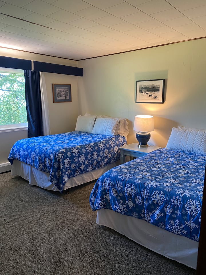 Upstairs bedroom with 2 full size beds. The bedroom has an en suite bathroom attached that has a shower and single vanity sink. 