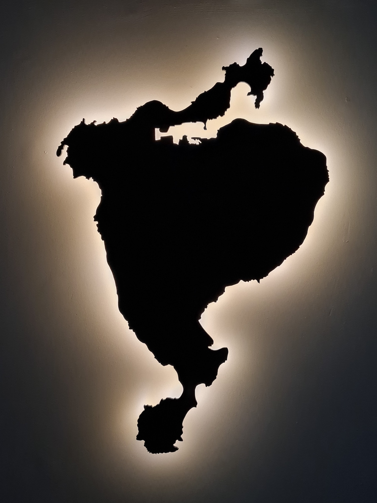 A decorative light fixture outlines the silhouette of an island map against a dark wall. The edges are illuminated softly, creating a striking contrast that highlights the island's form.