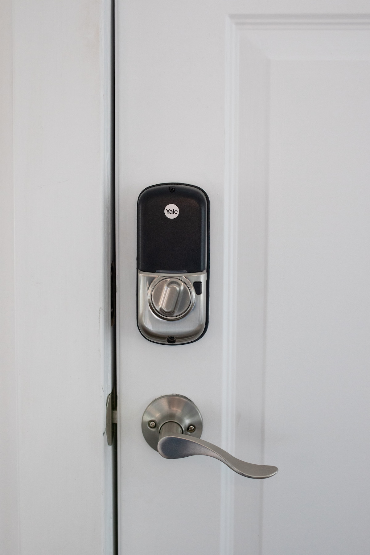 A secure door is featured, equipped with a Yale smart lock. A metallic door handle is positioned below the lock, both highlighting a modern and functional entrance. The door's finish presents a clean and contemporary appearance.