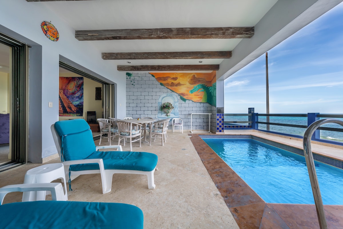 A spacious terrace features a private splash pool and comfortable lounge chairs. The area is adorned with a colorful mural, and a dining table is set nearby for outdoor meals. Expansive sliding doors provide beautiful views of the ocean.