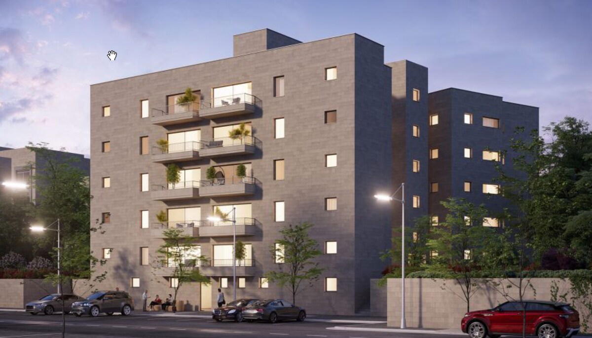 A modern apartment building is presented in a muted gray stone facade, highlighted by several balconies adorned with greenery. Soft lighting emanates from the windows, contributing to a warm ambiance. The surrounding area features landscaped greenery and a pathway lined with trees.