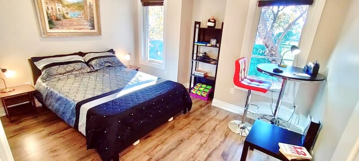 Master Bedroom ina bafu la suti, kitanda cha ukubwa wa malkia, meza ya ofisi, madirisha 2 marefu na vipofu vyeusi vinavyoangalia sehemu iliyo wazi kwenye ua wa nyuma.