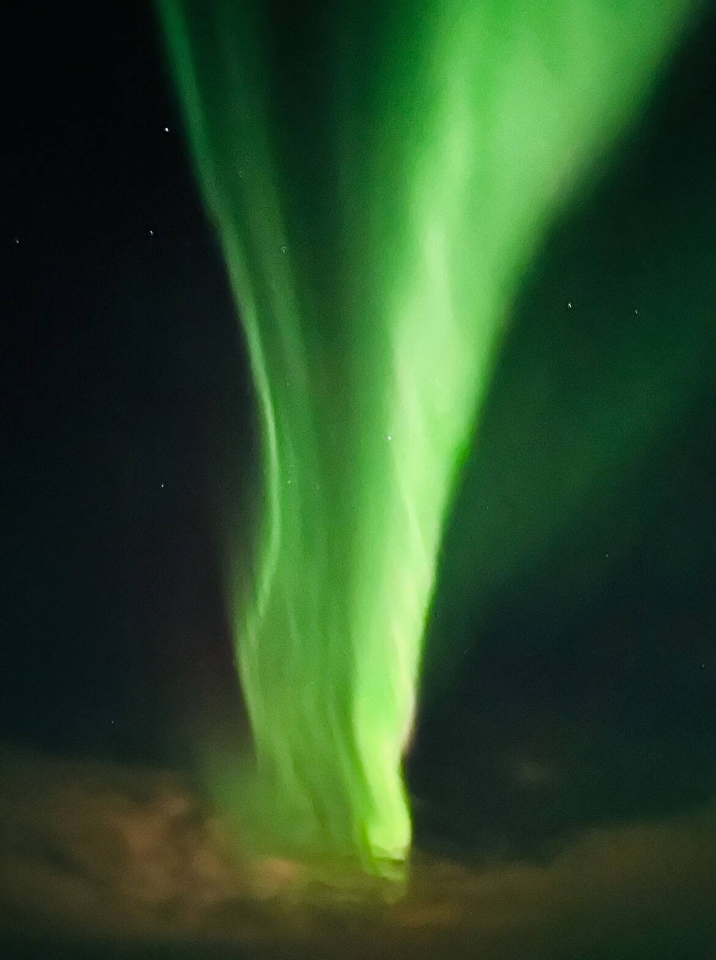 A vivid display of the Northern Lights illuminates the night sky, with green hues flowing gracefully across the darkness. The colors radiate in soft waves, creating a serene and captivating visual experience.