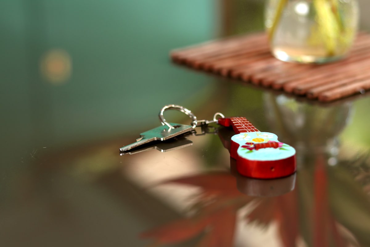 A decorative keychain shaped like a guitar is positioned next to a standard key. The scene is set atop a reflective surface, with soft lighting highlighting the intricate details and colors of the keychain.