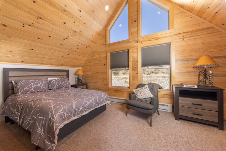 Relax in this serene upstairs retreat with a plush queen sized bed, cozy reading nook, and stunning A-frame windows that fill the room with natural light and mountain charm.