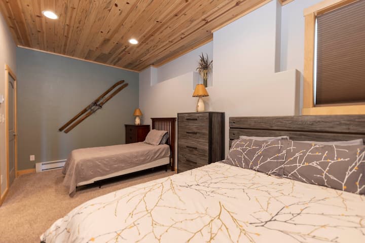 Unwind in this cozy, rustic-chic bedroom featuring wood-accented ceilings, comfy beds, and charming alpine decor—perfect for relaxing after a day of mountain adventures.  Queen and twin beds in basement floor.  