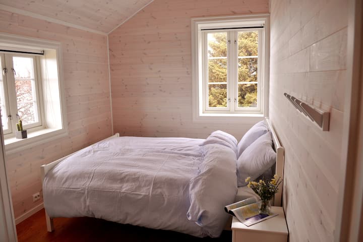 Спална соба со два прозорци и брачен кревет со поглед на Болга и морето на запад.