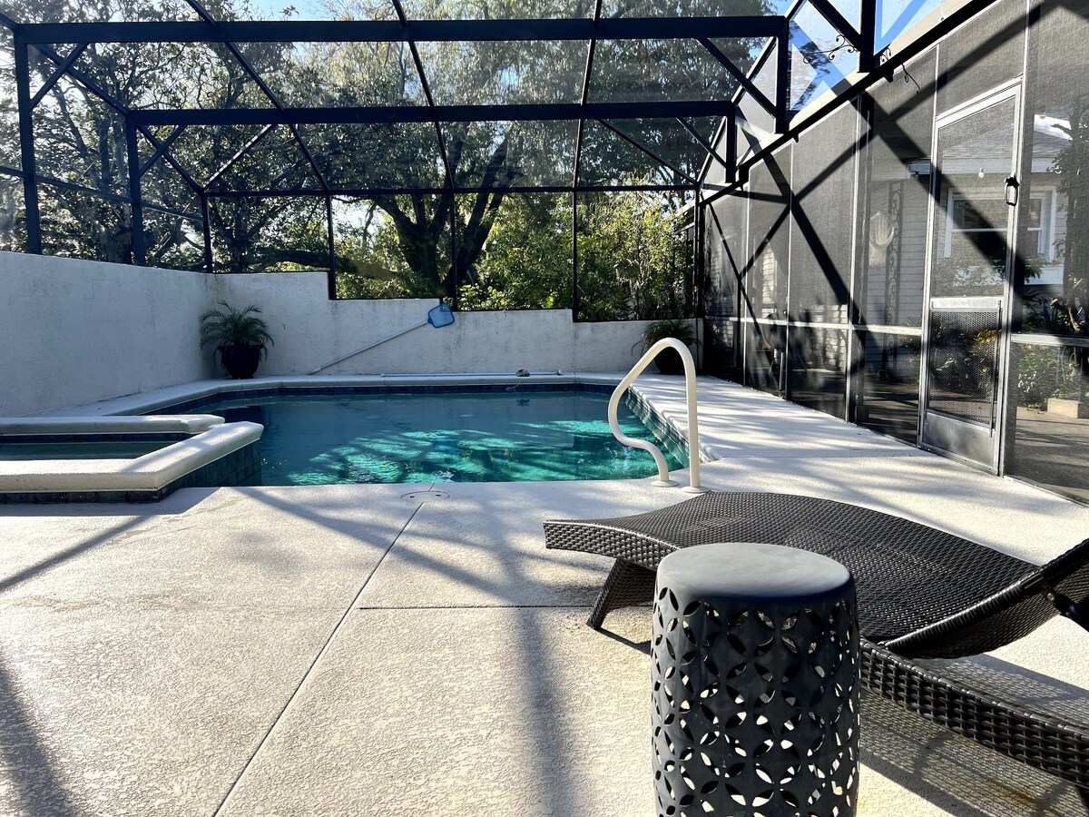 The private courtyard features a swimming pool surrounded by a protective screen enclosure. A hot tub is positioned beside the pool, with a lounge chair nearby. Sunlight filters through the enclosure, highlighting the space's inviting atmosphere.