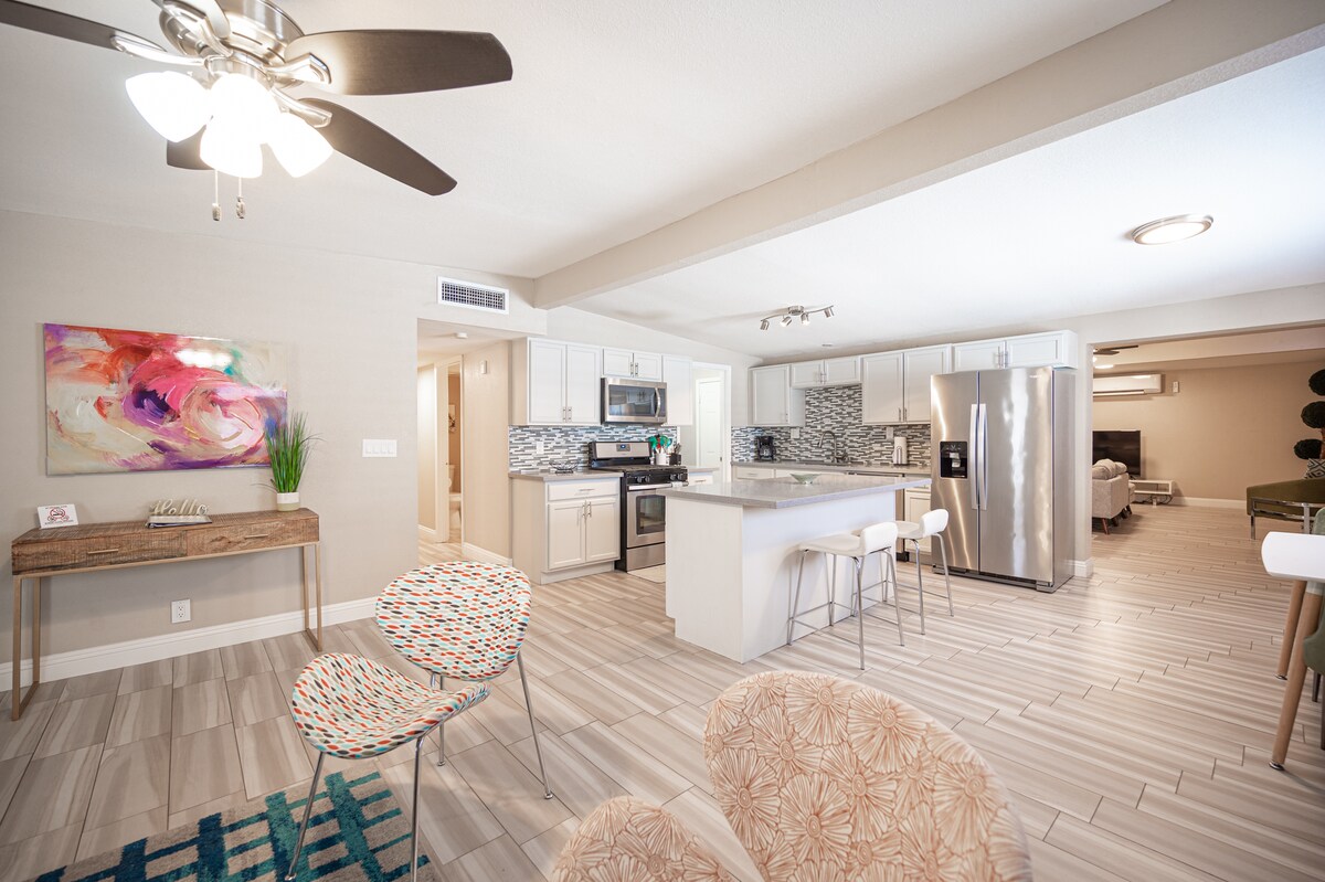 An open-concept kitchen and living area showcase modern appliances and a spacious layout. Colorful accent chairs add a touch of style, while natural light fills the room through ample windows. The neutral tones of the cabinetry and countertops create a calming atmosphere.