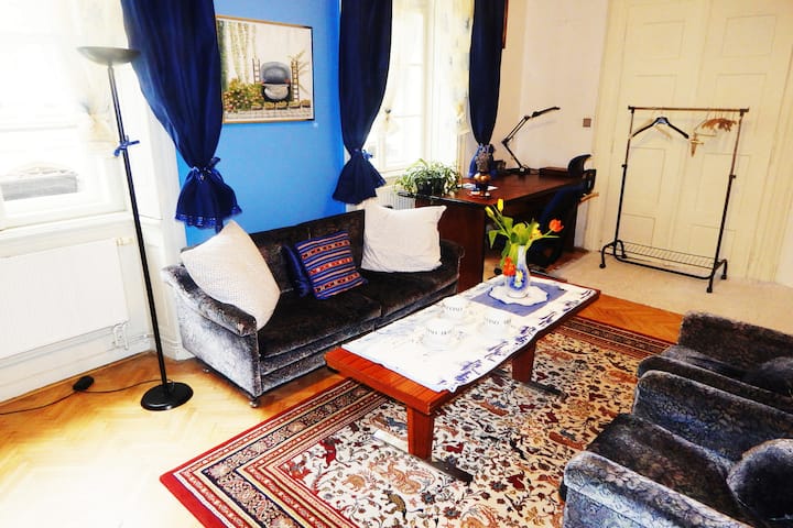 Всекидневна с третото легло, разположено до стената, което е противоположно на дивана с масата.