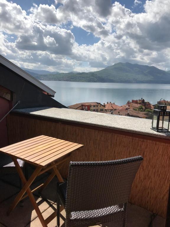 A small wooden table paired with woven chairs is positioned on the terrace, offering a panoramic view of the lake and surrounding mountains. The sky is filled with fluffy clouds, reflecting a serene atmosphere. The railing provides a sense of privacy while enjoying the outdoors.