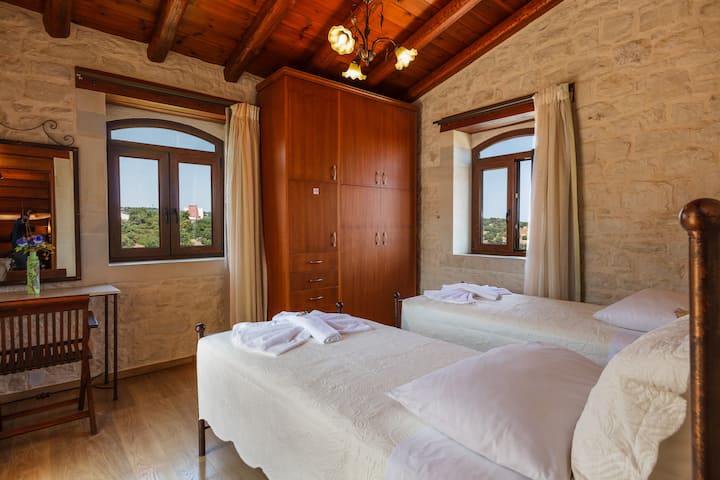 First-floor bedroom featuring two single beds that can be joined into a king-size bed upon request, with private balcony access offering views of Crete’s highest mountain.