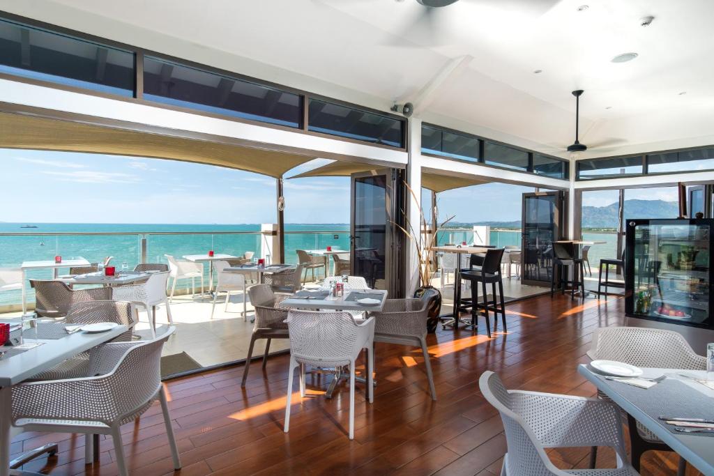 A modern dining area is featured with large windows that offer expansive views of the ocean. Stylish tables and chairs are arranged on a polished wooden floor, inviting guests to enjoy meals in a bright and airy atmosphere. Soft natural light enhances the open space.