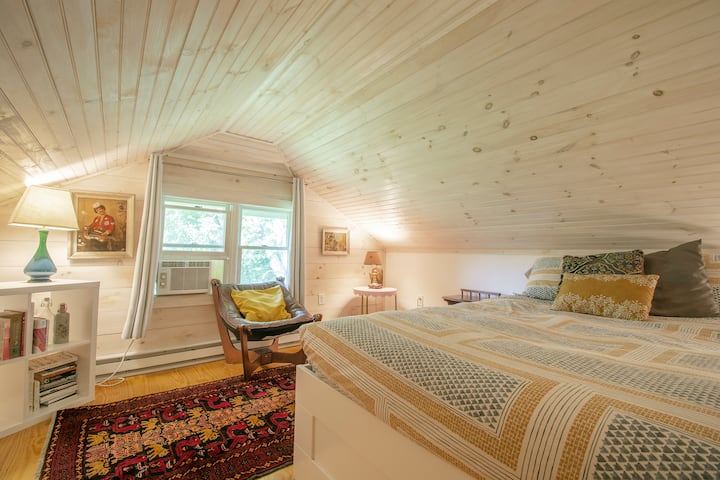 C'est la « Wood Room ».  C'est la meilleure chambre de la maison  Même mon père, qui mesure 6' 1", adore dormir dans la chambre au plafond en pente.  Cette chaise en face d'une fenêtre s'appelle une « chaise Luna ».  C'est un design scandinave vintage.