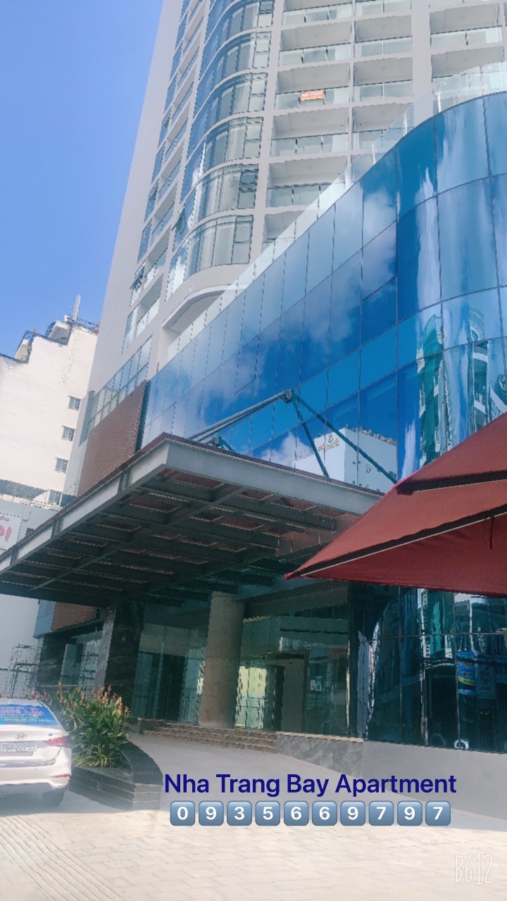 A modern building featuring a sleek glass facade reflects the surrounding environment. The entrance is marked by an awning, providing shade to the area below. Clear blue skies complement the contemporary architectural design.