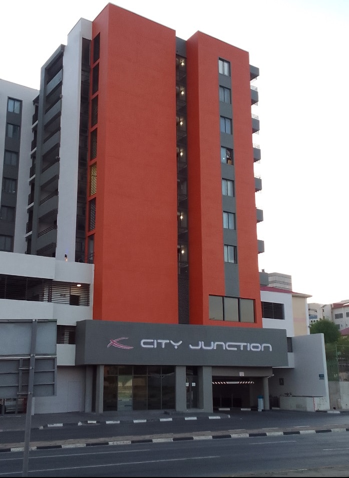 A modern multi-story building is showcased, featuring a blend of vibrant orange and grey exterior. The main entrance is marked by a prominent sign displaying 'City Junction,' with large windows visible on each floor.