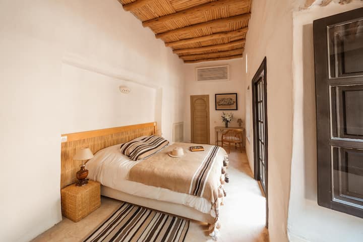 Habitación elegante Tagadert Lodge con vistas al patio, cama doble grande, decoración en colores beige, mantas y alfombras bereberes, grandes ventanas, persianas opacas. escritorio.