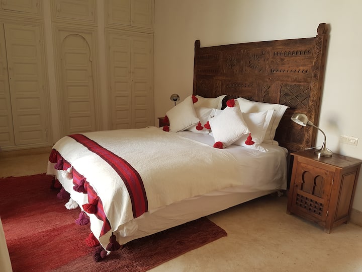 Habitación elegante con vistas a la piscina y al jardín de Tagadert Lodge, de colores rojos.
Alfombras y mantas artesanales marroquíes. Armarios, escritorio, aire acondicionado, hervidor de agua.
Habitación con terraza privada, cómodos sofás exteriores.