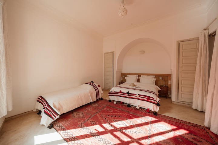 Elegante habitación Tagadert Lodge con vistas al jardín y al patio, con colores rosados.
1 cama doble grande + 1 cama individual. Armarios, aire acondicionado, terraza privada con vistas al jardín.
Hervidor de agua, oficina.