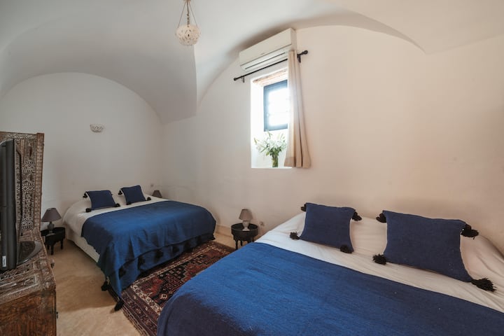 Elegante habitación familiar de colores azules: 2 camas dobles, armarios empotrados, aire acondicionado, terraza privada con vistas al patio común. Única habitación de Tagadert Lodge con TV y reproductor de CD.