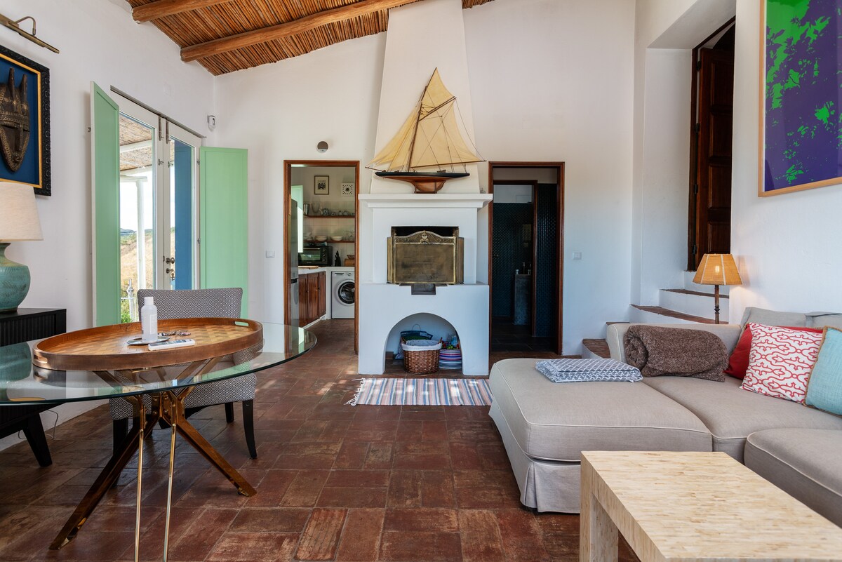 A cozy living area is highlighted by a modern sectional sofa and a wooden dining table. A decorative sailboat rests above a fireplace, with natural light flooding in from large glass doors that open to the views outside. Soft furnishings add comfort and warmth.