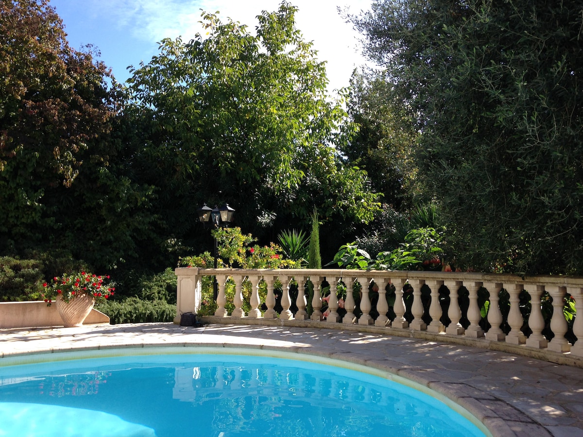 A serene view of a private pool surrounded by lush greenery, set within a well-kept garden. Elegant stonework outlines the pool, and vibrant flowers accentuate the area, enhancing the tranquil outdoor environment.
