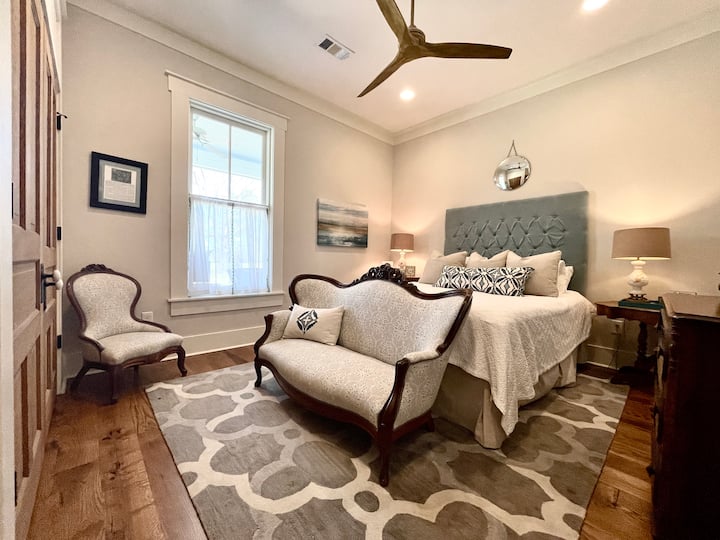 Предна стая за гости с олимпийско двойно легло (по - голямо от кралица и малко по - малко от двойно легло).  Прозорецът е с изглед към верандата и красивата горичка от дъбови дървета.