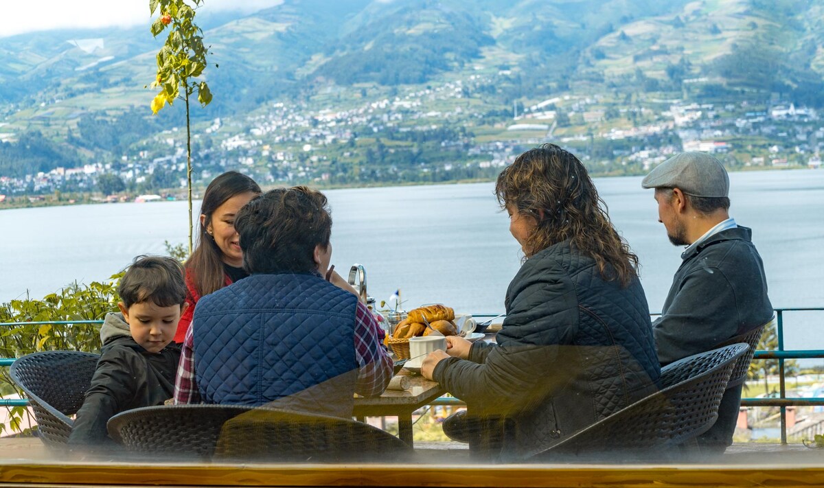 A table is set outdoors for a group enjoying snacks, with the serene Lake San Pablo in the background. Spectacular views of the surrounding hills and clear blue skies are visible, enhancing the experience of this calm outdoor dining area.