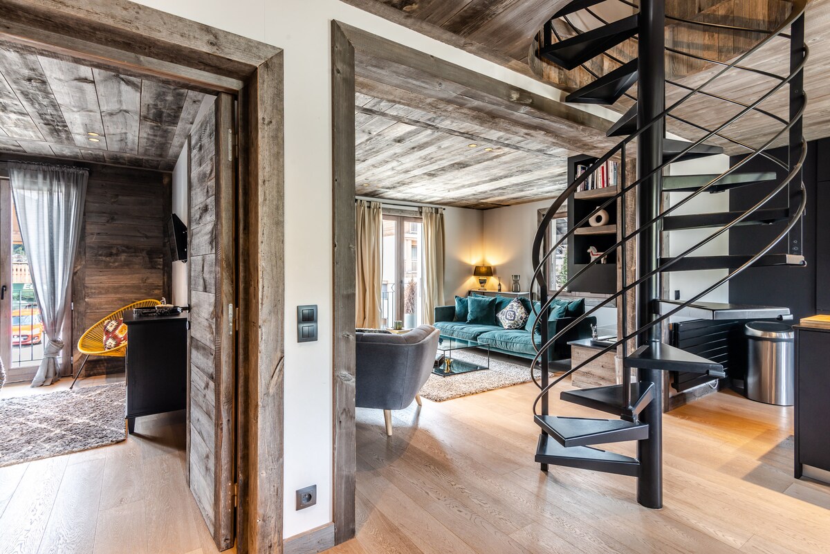 View of the open living space featuring a spiral staircase leading to the upper level. A cozy seating area is highlighted by a plush sofa and decorative furnishings. Natural light enters through large windows, with access to a balcony visible in the background.