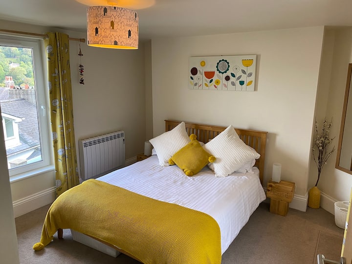 Chumba cha kulala cha mfalme wa ghorofani kilicho na mwonekano juu ya marina hadi kwenye maji. Upande wa kushoto pia kuna meza thabiti ya kuvaa mwalika iliyo na kikausha nywele.  Kwa upande wa kulia ni bafu kubwa la chumbani lenye bomba la mvua na bafu tofauti.