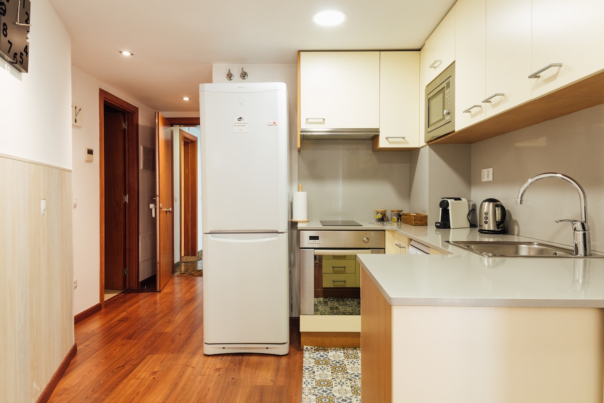 The kitchen features modern cabinetry and a clean countertop with essential appliances. A refrigerator and a small oven are visible, alongside a kitchen sink and counter space. Decorative tiles add a touch of character to the floor. Warm wood accents enhance the welcoming atmosphere.