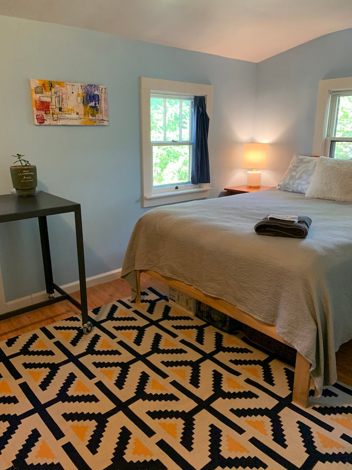 Bedroom 2 has a queen bed, and a tall desk in the corner. The desk is in front of a door that leads to the backyard.  