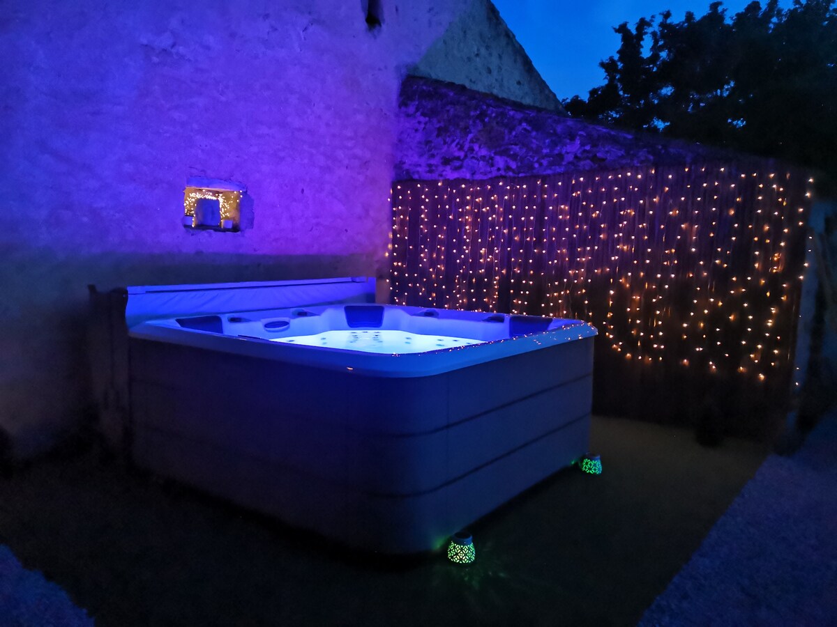 A hot tub is illuminated with soft blue lighting, surrounded by a stone wall and adorned with twinkling fairy lights. The scene is set in a tranquil outdoor area, enhancing the peaceful ambiance of the property.