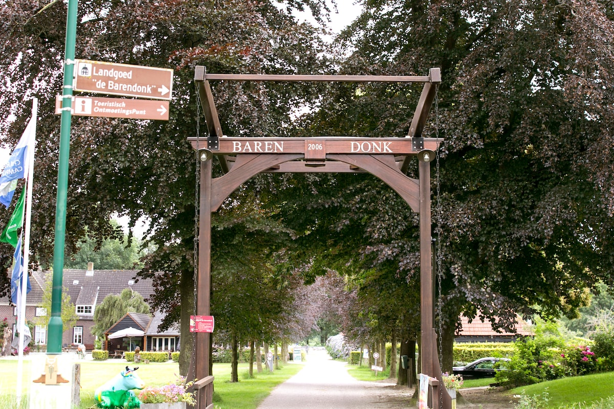 A wooden archway marked with 'Baren Donk' stands at the entrance, framed by tall trees and greenery. Signposts direct visitors towards 'Landgoed de Barendonk' and 'Fietsenstalling', guiding the way into the estate's serene surroundings.